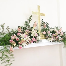 Pink and white floral arrangement with lilies and roses around a gold cross