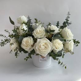 White roses arranged in a white vase with eucalyptus greenery