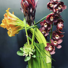 Arrangement of orchids, calla lilies, and a succulent in a tall vase