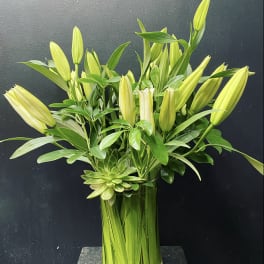 Tall arrangement of unopened yellow lilies in a glass vase