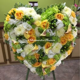 Heart-shaped floral arrangement with yellow roses, white blooms, and calla lilies on an easel