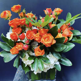 Orange roses arranged in a clear glass vase with white flowers