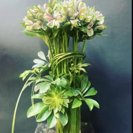 Tall bouquet of pale pink and white flowers with green foliage in a clear vase