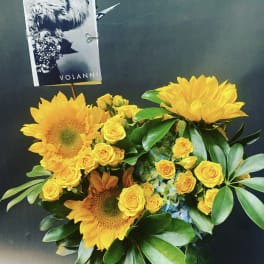 Yellow sunflowers and roses in a glass vase with a card pick