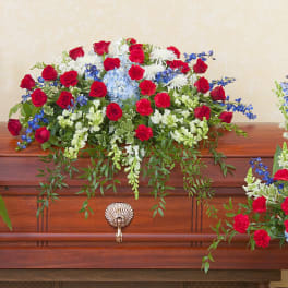 Red, white, and blue funeral flowers arranged around a wooden casket.