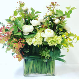 White flowers in a clear square vase with green foliage and red berry accents
