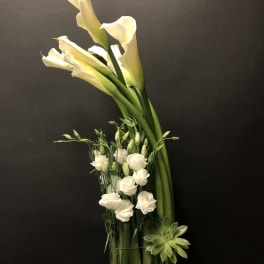 White calla lilies and small white blooms in a glass vase