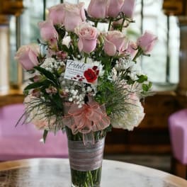 Pink roses arranged in a clear glass vase with a pink ribbon bow