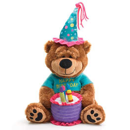 Plush teddy bear wearing a birthday hat and shirt, holding a cake