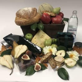 Gift basket with bread, fruit, cheese, cookies, flowers, and a bottle of sparkling water