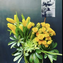 Yellow tulips and roses in a glass vase with green foliage