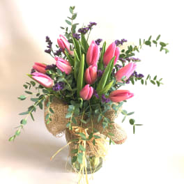 Pink tulips arranged in a burlap-wrapped vase with purple filler flowers