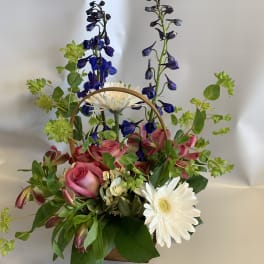 Basket arrangement with pink roses, white daisies, and blue flowers