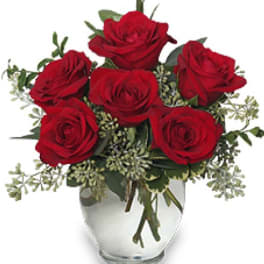Red roses arranged in a clear glass vase with greenery