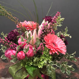 Pink and purple floral arrangement in a glass vase with a green ribbon