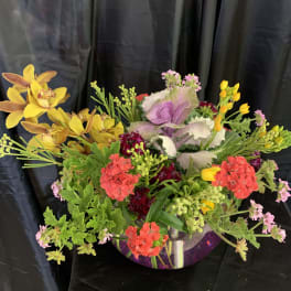 Mixed floral arrangement in a clear glass bowl with yellow orchids and pink blooms