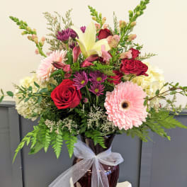 Mixed bouquet of roses, lilies, and daisies in a vase with a white ribbon