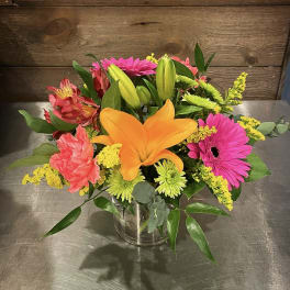 Mixed bouquet with orange lily, pink gerberas, and yellow filler in a glass vase
