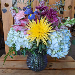 Mixed bouquet in a dark glass vase with yellow, pink, purple, and blue flowers
