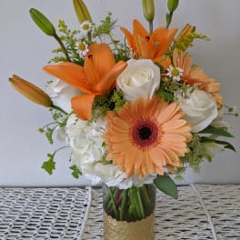Orange lilies and peach gerbera daisies in a glass vase with white roses