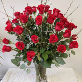 Red roses arranged in a clear glass vase with branching accents