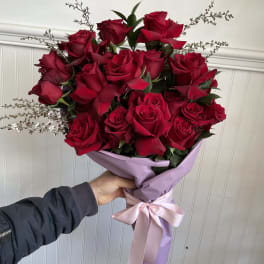 Bouquet of red roses wrapped in lavender paper with a pink ribbon