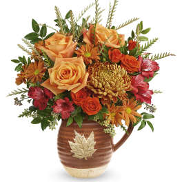 Orange roses and chrysanthemums in a brown leaf-accented pitcher vase