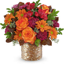 Orange and red mixed flower arrangement in a gold textured vase