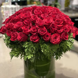 Large dome of red roses with a green foliage collar in a clear glass cylinder vase.