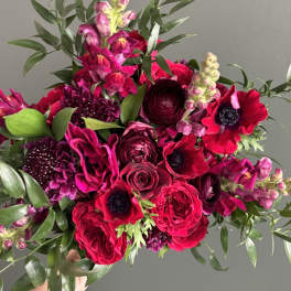 Handheld bouquet of hot pink and burgundy flowers with greenery
