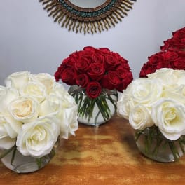 Three rose arrangements in clear glass bowls, in red and white.