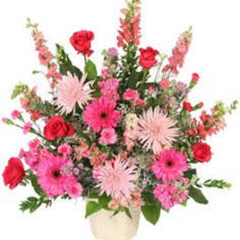 Pink and red mixed flower arrangement in a cream ceramic container