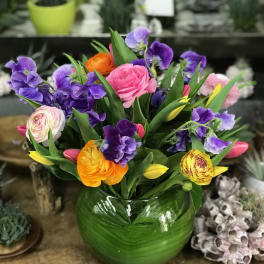 Colorful bouquet of pink, purple, yellow, and orange flowers in a green glass vase