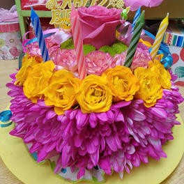 Bright pink and yellow floral birthday cake with candles and ribbon