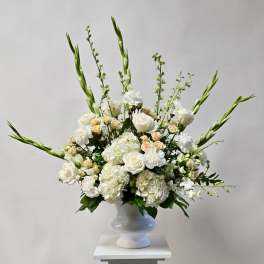 White floral arrangement in a white pedestal vase with tall green spikes