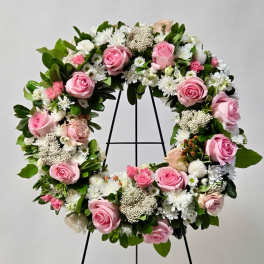 Pink roses and white flowers arranged in a circular wreath on a stand