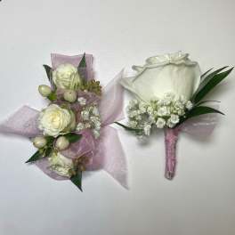 Two white floral boutonnieres with pink ribbon and greenery