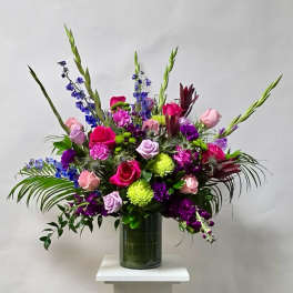 Tall mixed bouquet of roses, purple blooms, and green spikes in a glass vase