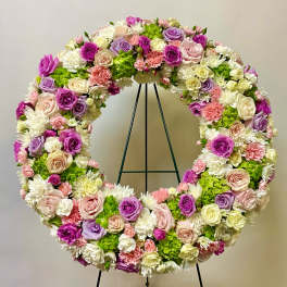 Large circular floral wreath with pink, purple, white, and green blooms on a stand