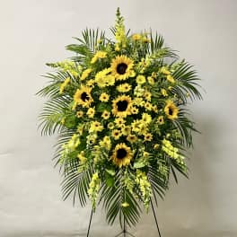 Standing floral spray with yellow sunflowers and daisies on a black easel