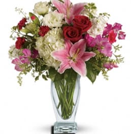 Pink lilies, red roses, and white blooms in a clear glass vase