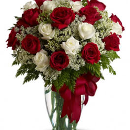 Red and white roses in a clear glass vase with a red ribbon