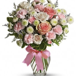 Pink and white rose bouquet in a glass vase with a pink ribbon