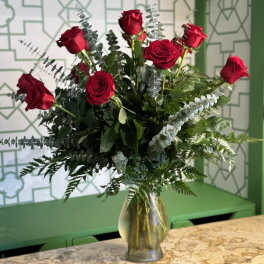 Red roses arranged in a clear glass vase with mixed greenery
