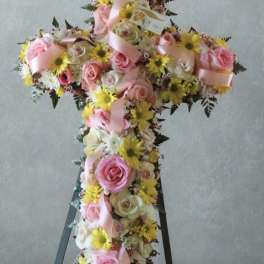 Cross-shaped floral arrangement with pink roses and yellow daisies on an easel