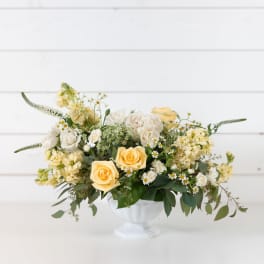 Cream and yellow floral arrangement in a white pedestal vase
