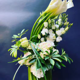 Tall white floral arrangement with calla lilies and roses in a glass vase