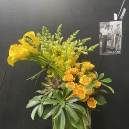 Yellow calla lilies and roses in a glass vase with greenery