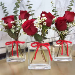Three small rose arrangements in square glass vases with red bows