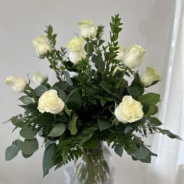 White roses arranged in a clear glass vase with mixed greenery